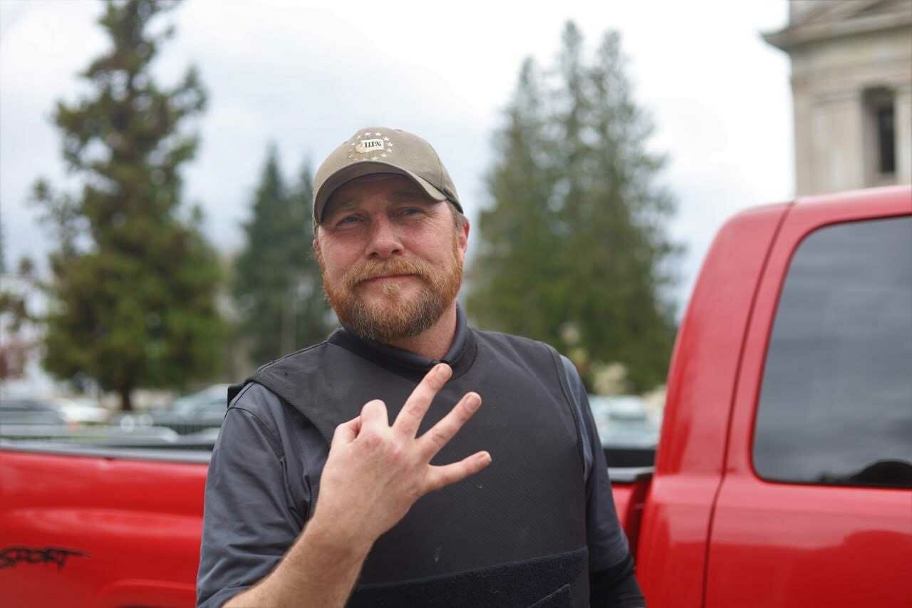 Three Percent of Washington vice-president Erik Rohde flashes the Three Percenter hand signal — meant to resemble a Roman numeral three. Extremism experts stress that it should not be confused with the “OK” sign used by some white nationalist groups.